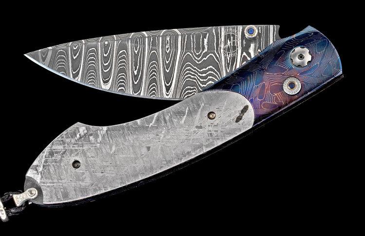 Partially open folding knife with Damascus blade and blue-purple titanium handle featuring meteorite inlay and a sapphire pivot.