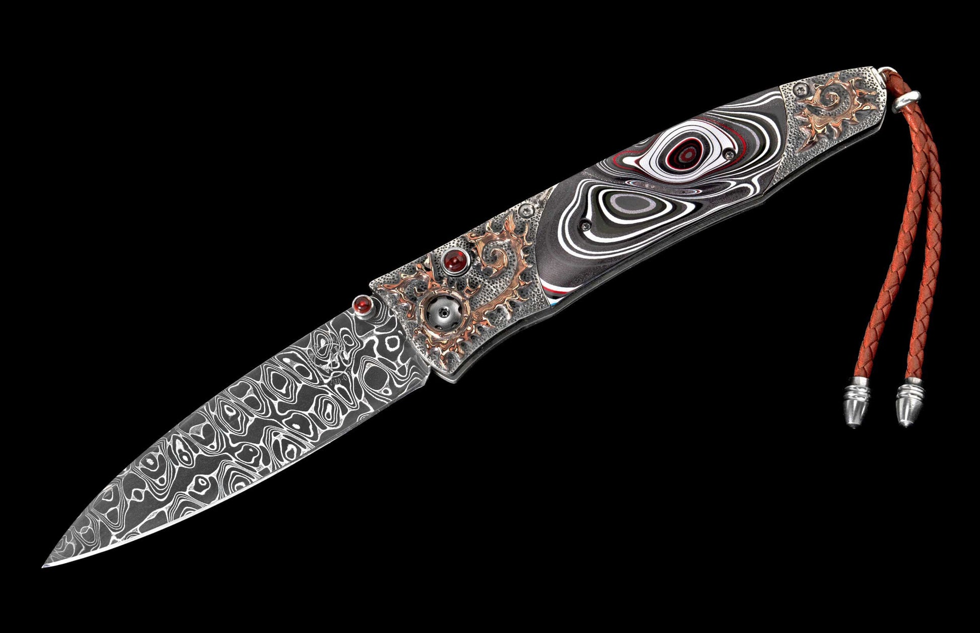 Ornate folding knife with Damascus blade, abstract black, white, and red handle, red gemstones, bronze metalwork, and a braided red leather lanyard.