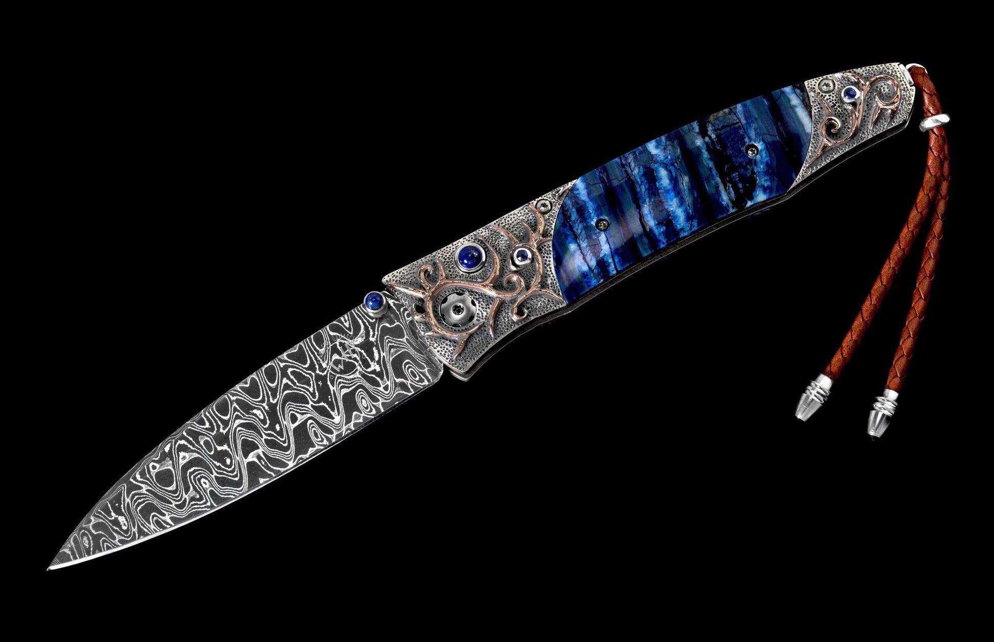 Decorative folding knife with Damascus blade, blue streaked handle, ornate silver and bronze bolsters with blue gems, and a brown leather lanyard.