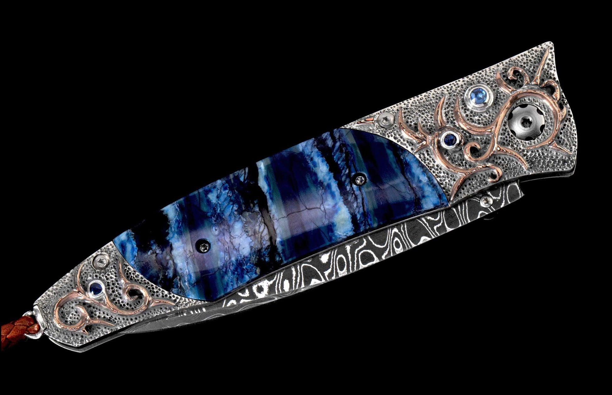 Ornate folding knife with vibrant blue stone handle, textured silver hilt featuring bronze swirls and blue gems, Damascus steel blade, and brown leather lanyard.