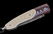 Custom folding knife with a carved cream handle featuring a scorpion motif, vibrant wavy patterned metal scale, and a Damascus blade.