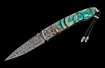 Ornate folding knife with a Damascus blade, teal and white handle scales, silver scrollwork, a gold skull, and red ruby accents.