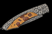 Decorative folding knife with burl wood handle, silver-toned floral engraved frame, and a Damascus steel blade.