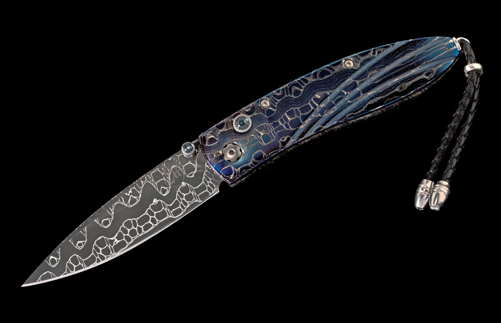 Folding knife with intricate patterned blade and a textured blue-purple handle, accented with a black braided lanyard.