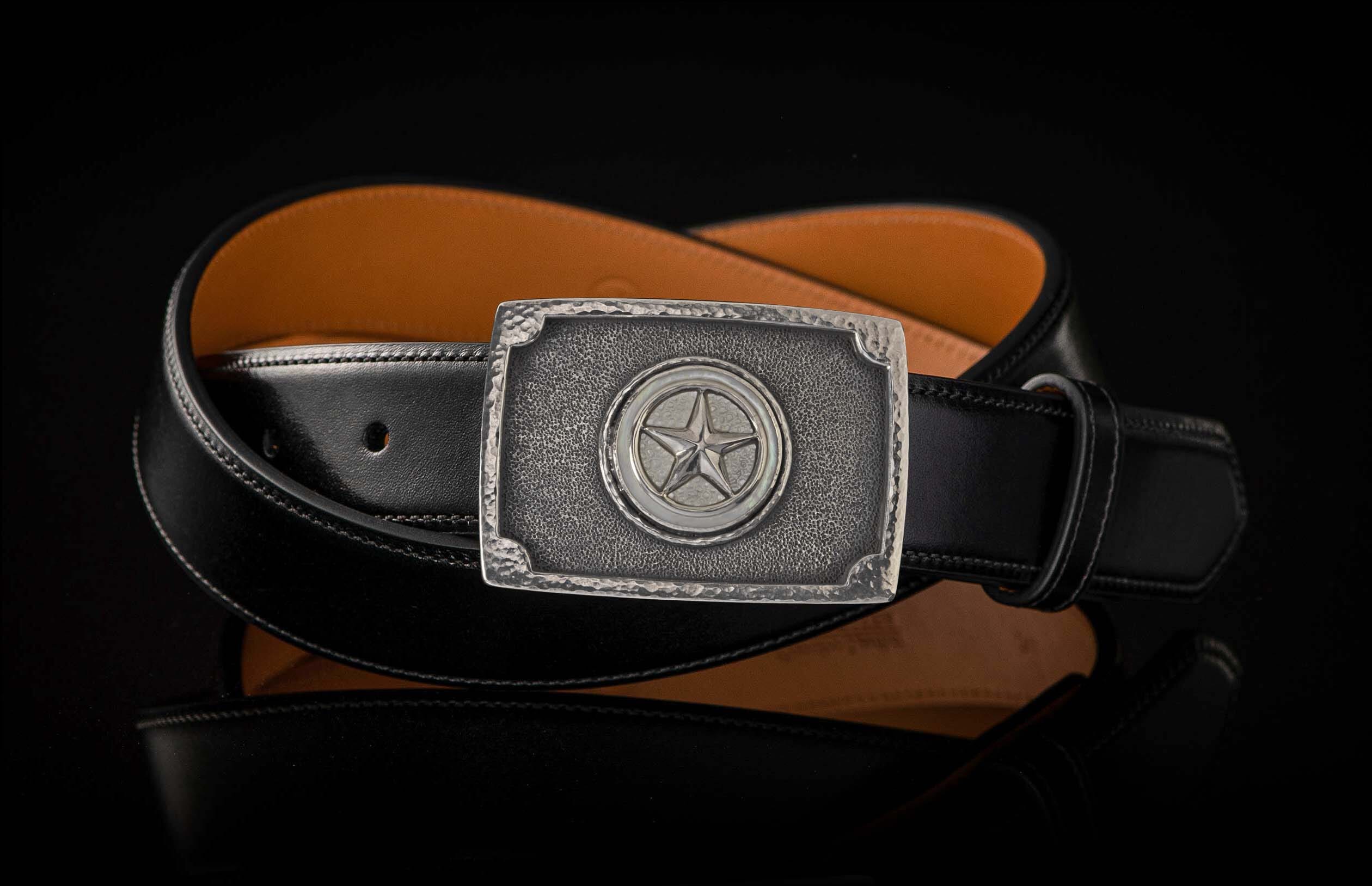 Silver metal buckle with hammered frame and central star, on a black leather belt with tan lining.