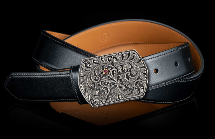 Silver-toned buckle with intricate scrollwork and a red gem, attached to a black leather belt.