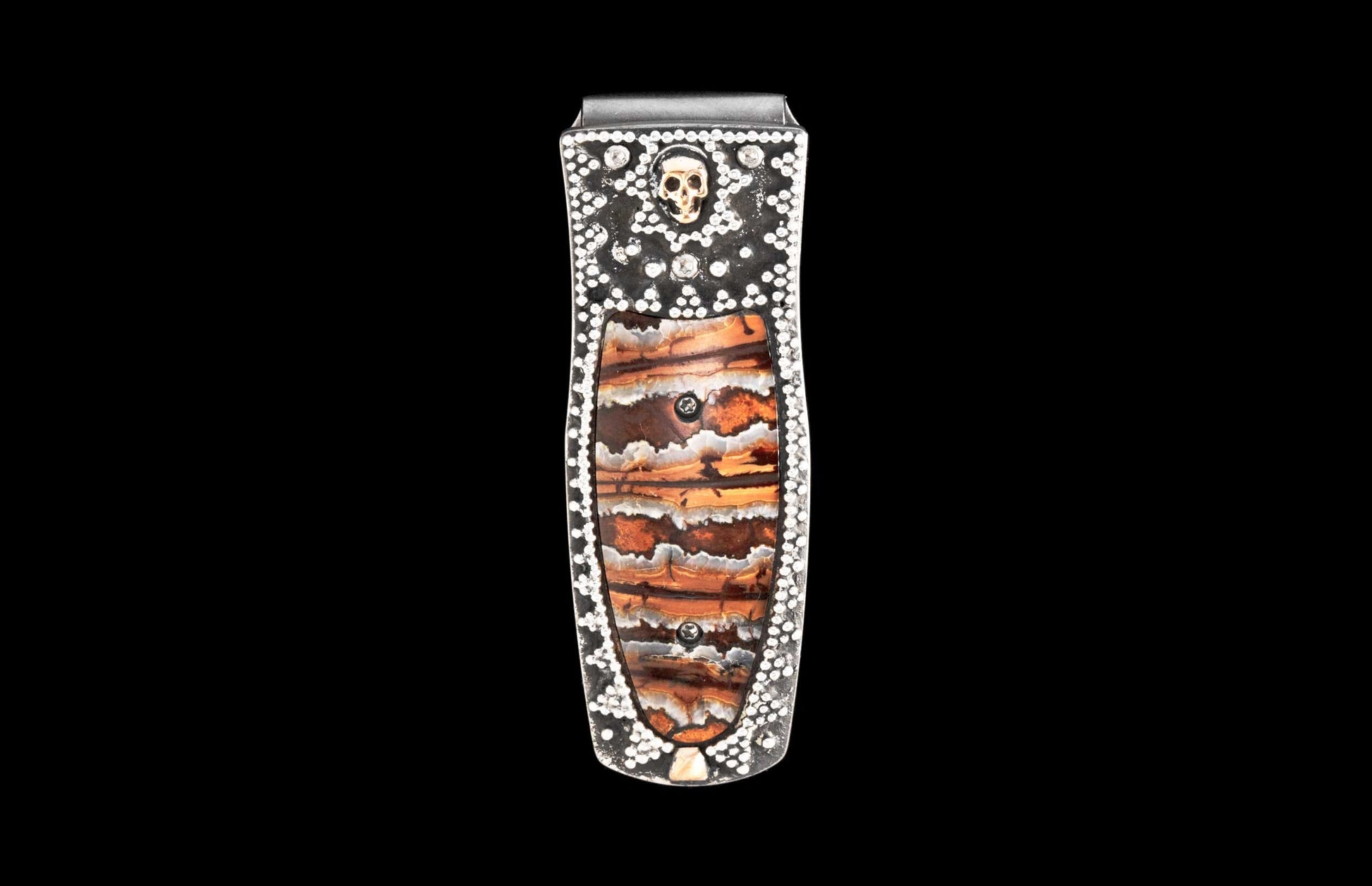 Silver-tone money clip featuring a layered brown and orange stone inlay, studded with white gems and a gold skull.