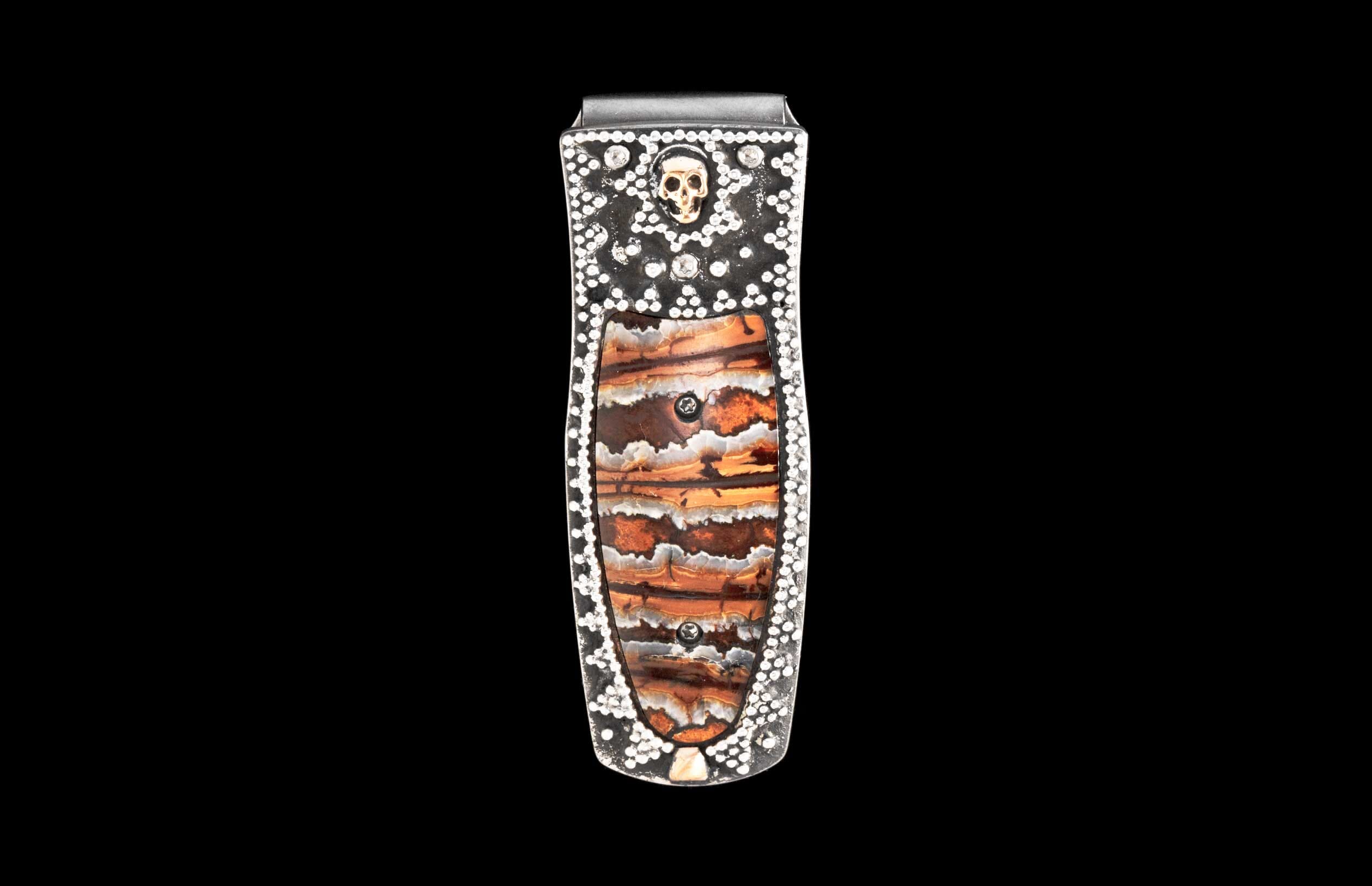 Silver-tone money clip featuring a layered brown and orange stone inlay, studded with white gems and a gold skull.