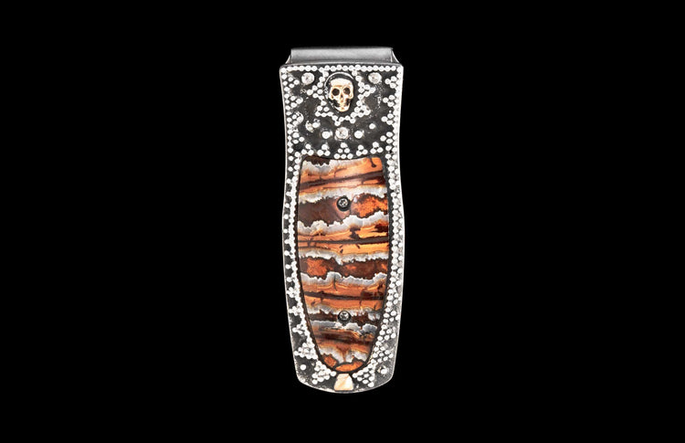 Silver-tone money clip featuring a layered brown and orange stone inlay, studded with white gems and a gold skull.