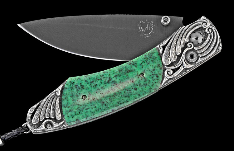 Folding knife with a green speckled stone handle, dark Damascus blade, and ornate silver bolsters with feather carvings and black accents.
