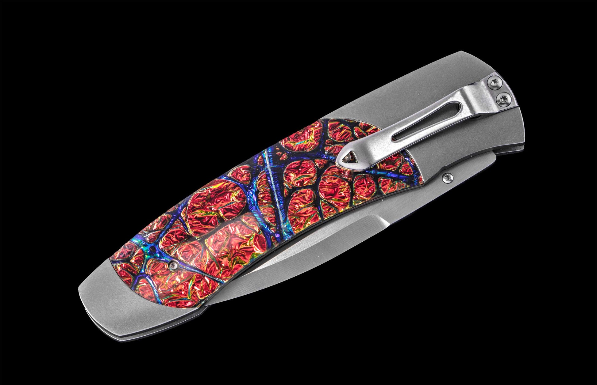Folding knife with vibrant red and blue mosaic patterned handle, stainless steel blade and clip, side view on black background