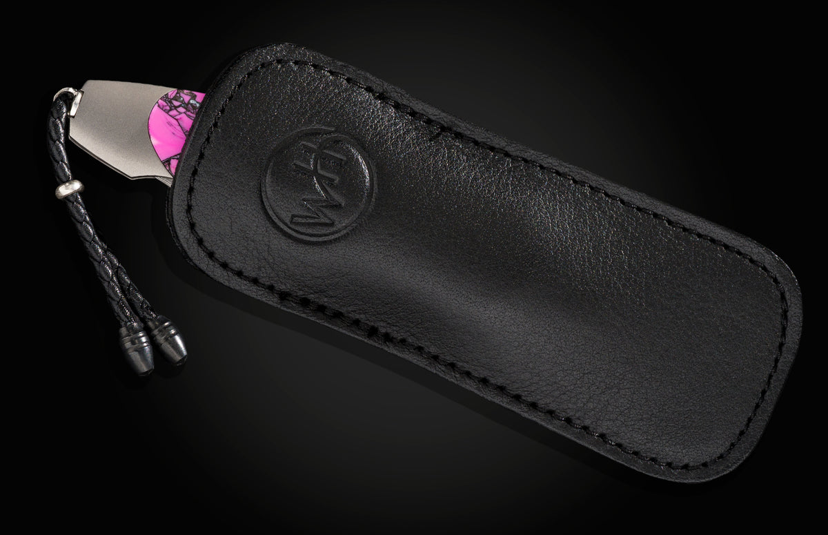 Luxury black leather knife sheath with embossed logo, featuring a silver-toned blade and vibrant pink camo handle, shown in side view.