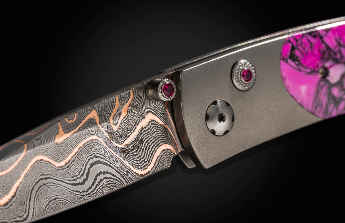 Damascus steel folding knife with rose gold wave pattern and pink gemstone accents, side view close-up