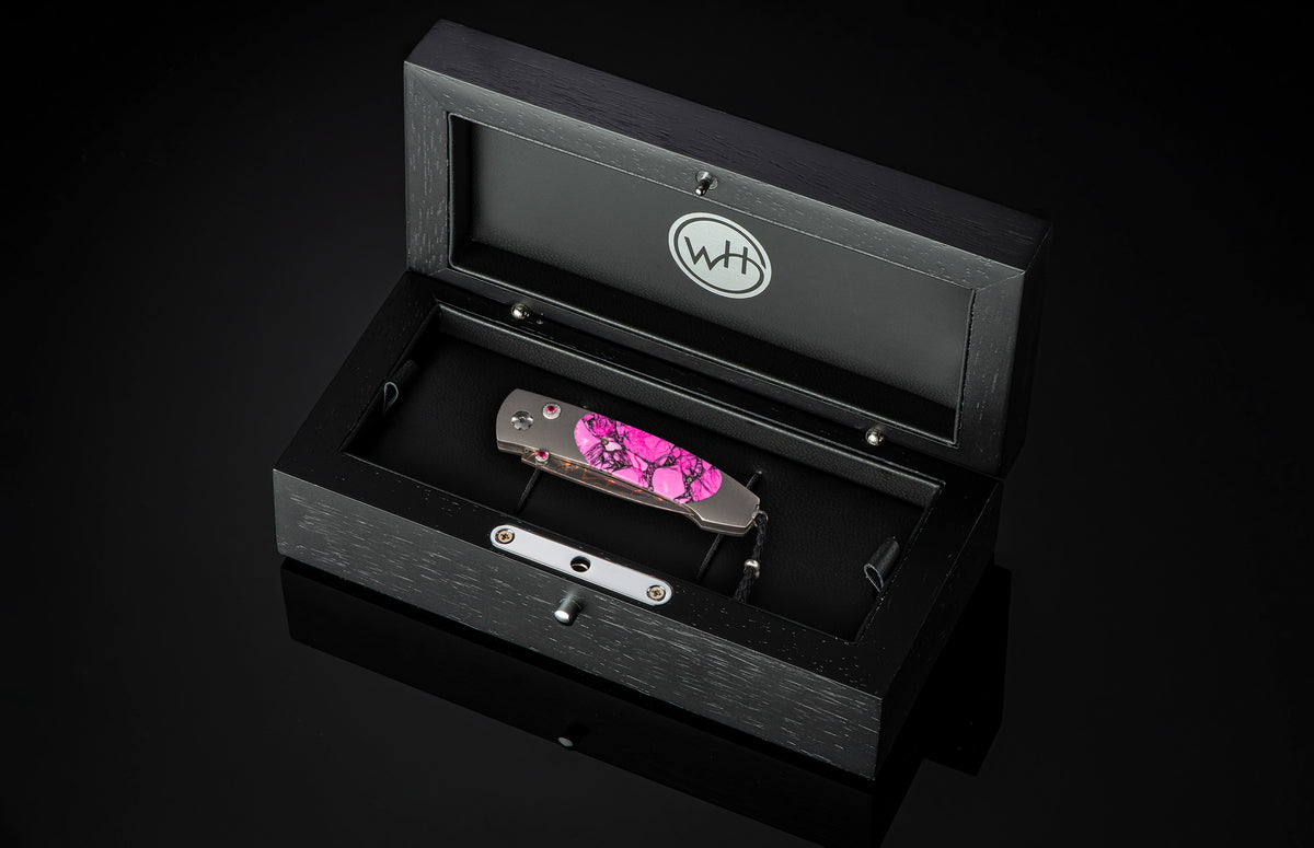 Luxury folding knife with vibrant pink marbled handle and polished silver hardware by W+H, displayed in a sleek black presentation box.