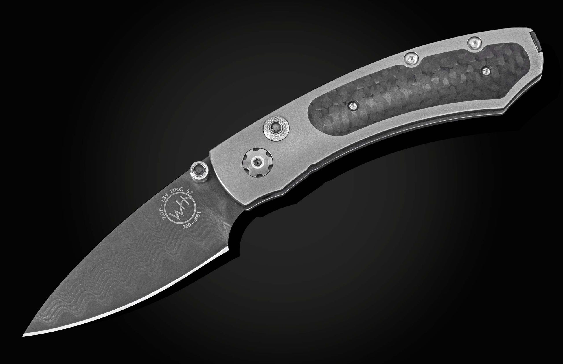 Grey folding knife with dark carbon fiber handle and wavy Damascus blade pattern, shown diagonally on black.