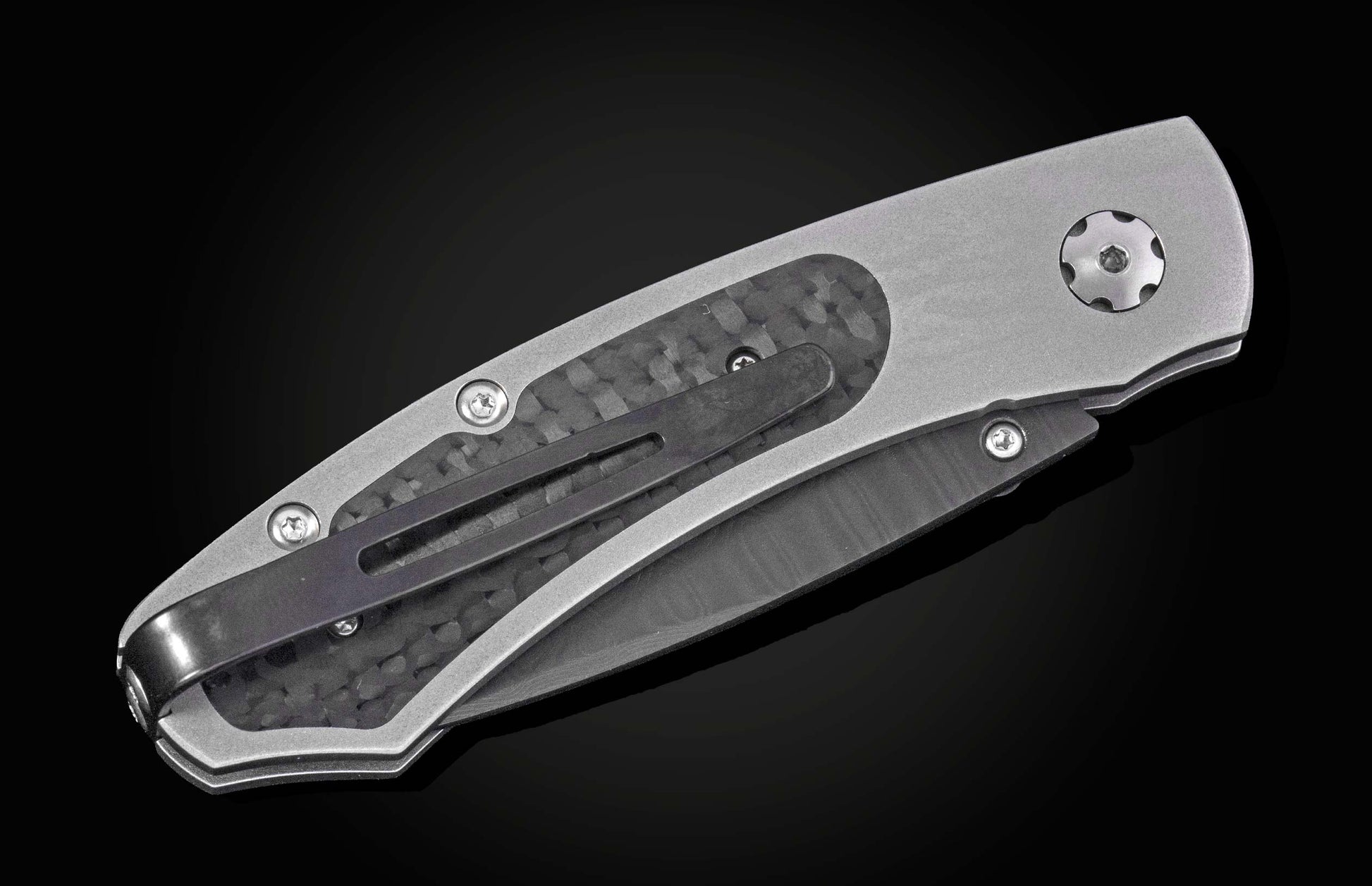 Silver-gray folding knife with carbon fiber inlay and dark pocket clip against a black background.