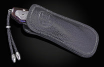 Folding knife with decorative handle in leather case on a black background