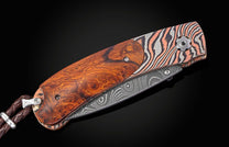 Folding knife with a decorative blade and desert ironwood handle on a black background with the blade closed