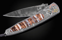 Damascus steel folding knife by B10 with engraved eagle head, amber inlay, and ornate silver handle, side view on black background