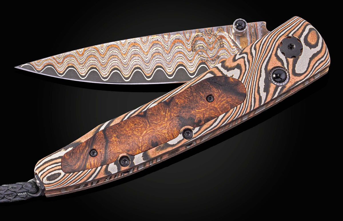 Damascus steel folding knife with wavy blade pattern and wood inlay handle, by B10 Riverwood, featuring black stone accents and braided lanyard, side view on dark background