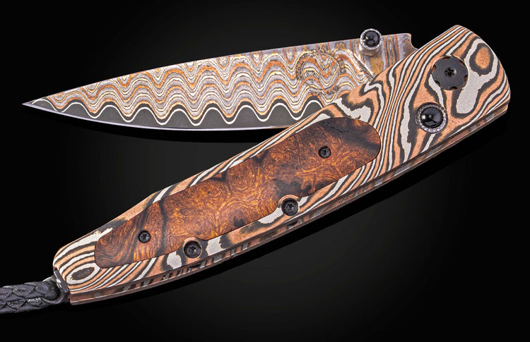 Damascus steel folding knife with wavy blade pattern and wood inlay handle, by B10 Riverwood, featuring black stone accents and braided lanyard, side view on dark background