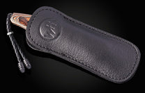 Luxury Riverwood knife with striped wood handle in black leather sheath by B10, featuring embossed logo and braided cord, side view on dark background