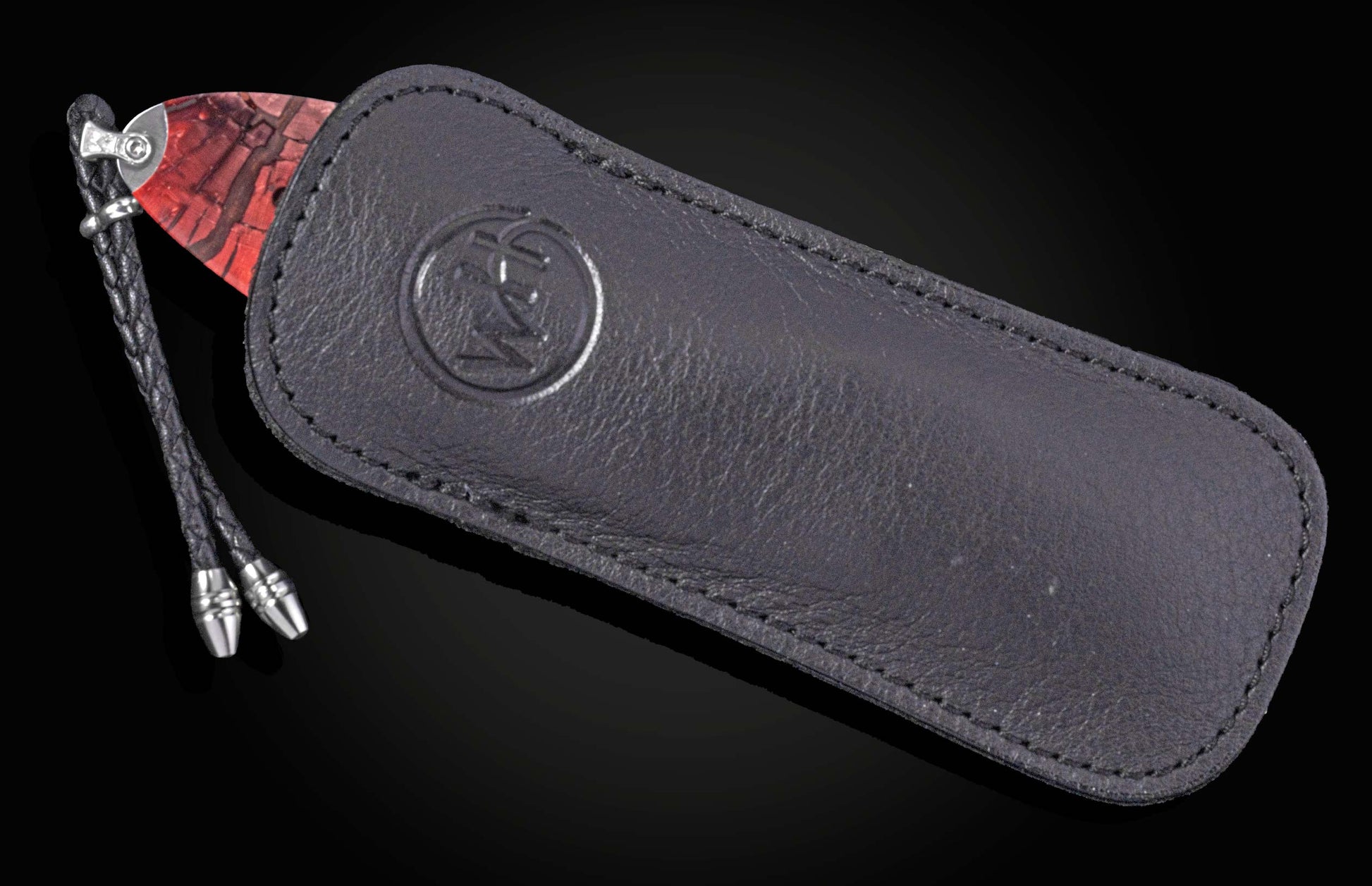 Folding knife with a red patterned handle, partially in a dark leather sheath with an embossed logo and braided lanyard.