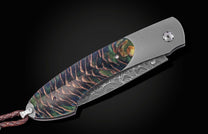 Luxury folding knife with iridescent Aurora Pine handle and damascus blade, side view on black background