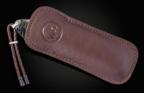 Luxury B12 Aurora Pine knife in dark brown leather sheath with embossed logo, braided cord, and iridescent handle, side view.