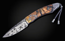 Ornate folding knife featuring a swirling Damascus steel blade, a carved leopard head handle, an elephant pommel, and a braided lanyard.