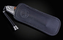 Folding knife with an embossed boar head handle, wood inlay, and braided lanyard, partly in a black textured leather sheath with an embossed logo.