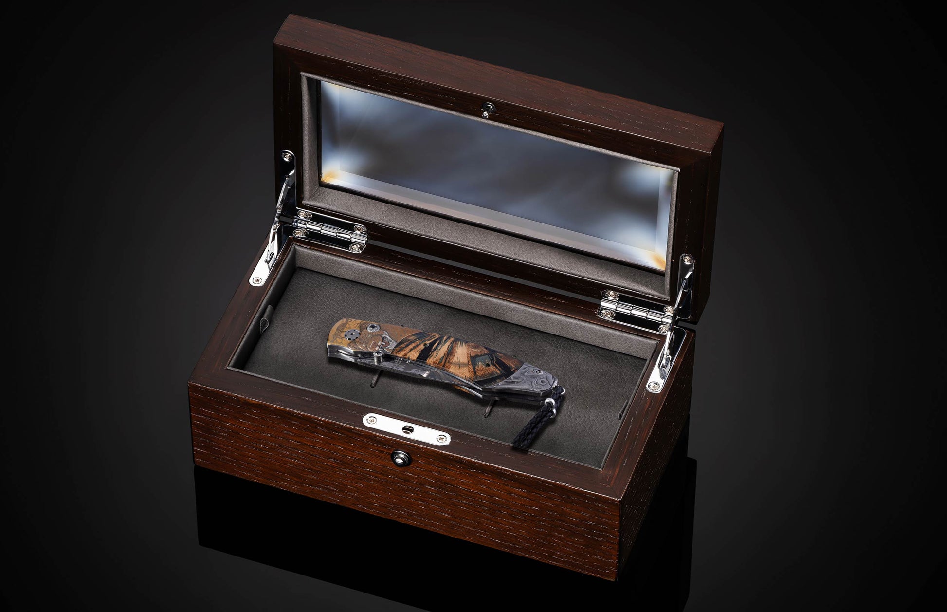 Folding knife with a carved Big 5 animal handle and striped wood inlay, displayed in an open dark wooden box.