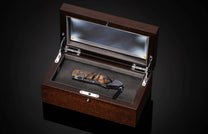 Folding knife with a carved Big 5 animal handle and striped wood inlay, displayed in an open dark wooden box.