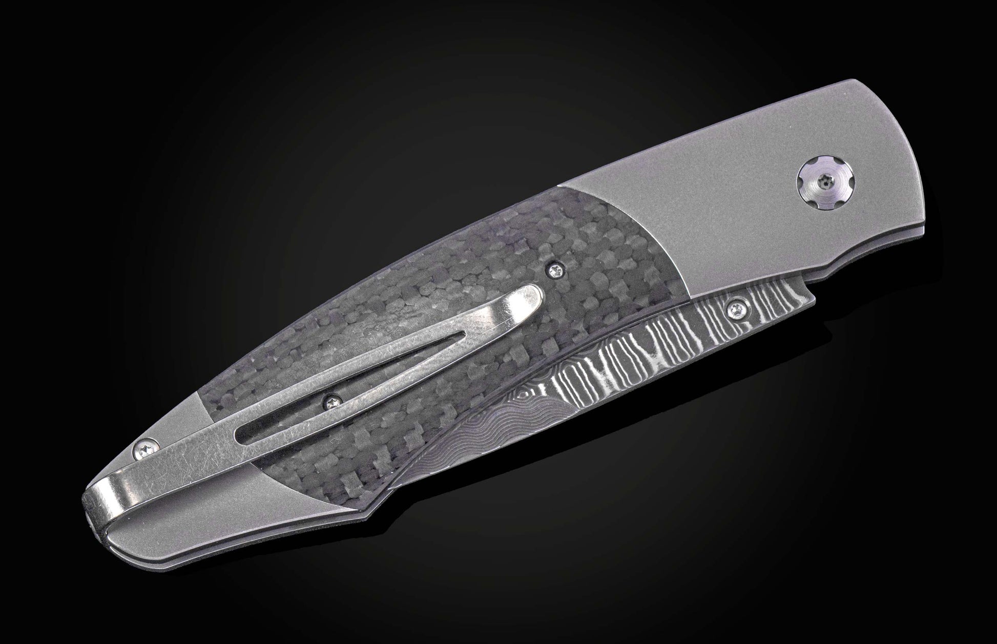 Closed folding knife with grey handle, carbon fiber inlay, wavy patterned blade, and pocket clip.
