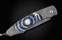 Luxury folding knife with blue and gold resin inlay, damascus steel handle, side view on black background
