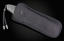 Damascus steel knife with blue meadow pattern in black leather sheath by B12, featuring braided cord and embossed logo, side view
