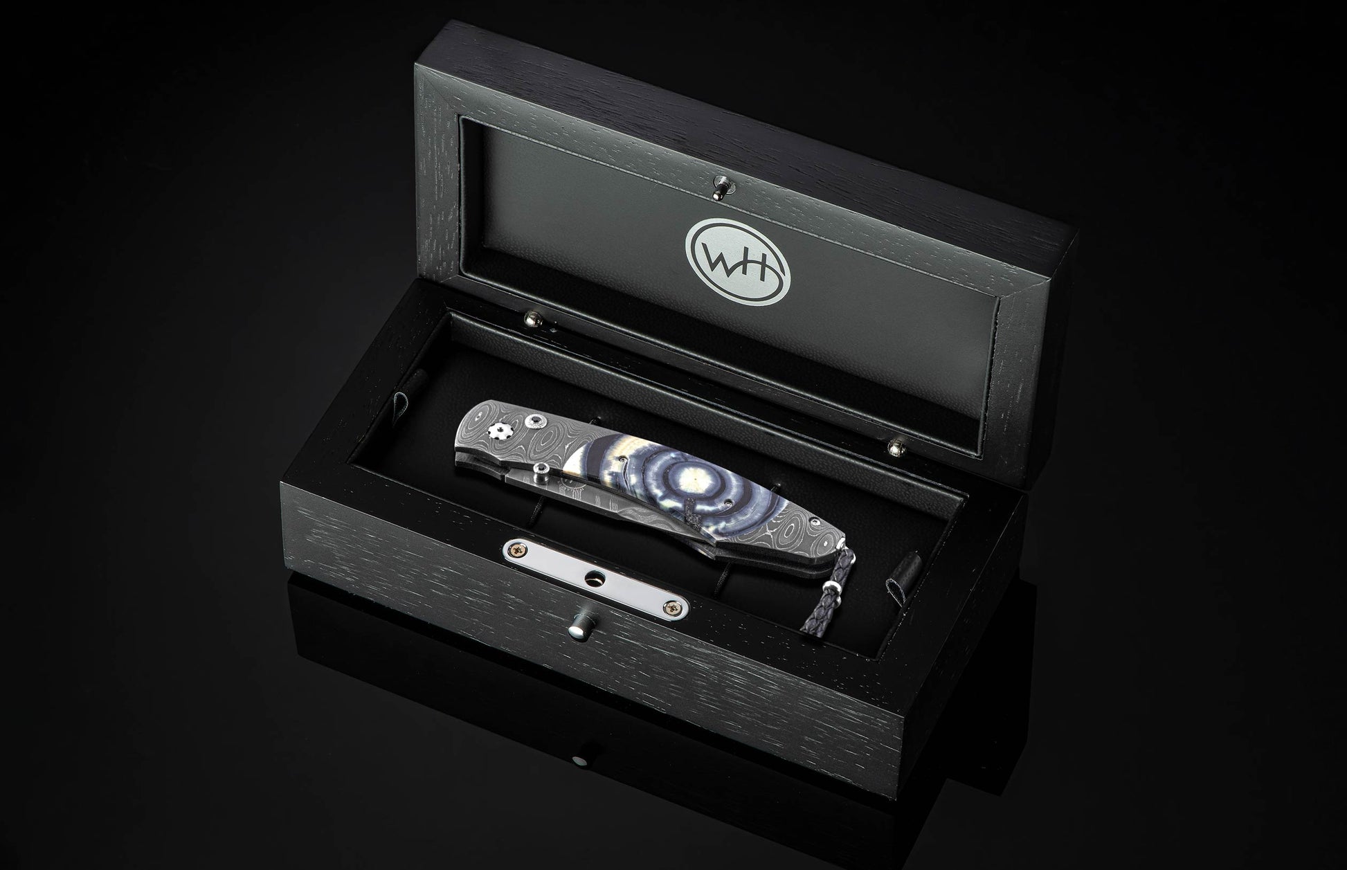 Luxury folding knife with blue and silver marbled handle by B12, displayed in black wooden box with engraved logo, top-down view
