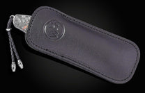 Luxury silver Chinese dragon knife with intricate engravings and red accents, by B12, in black leather sheath with braided cord and metallic tips, side view.