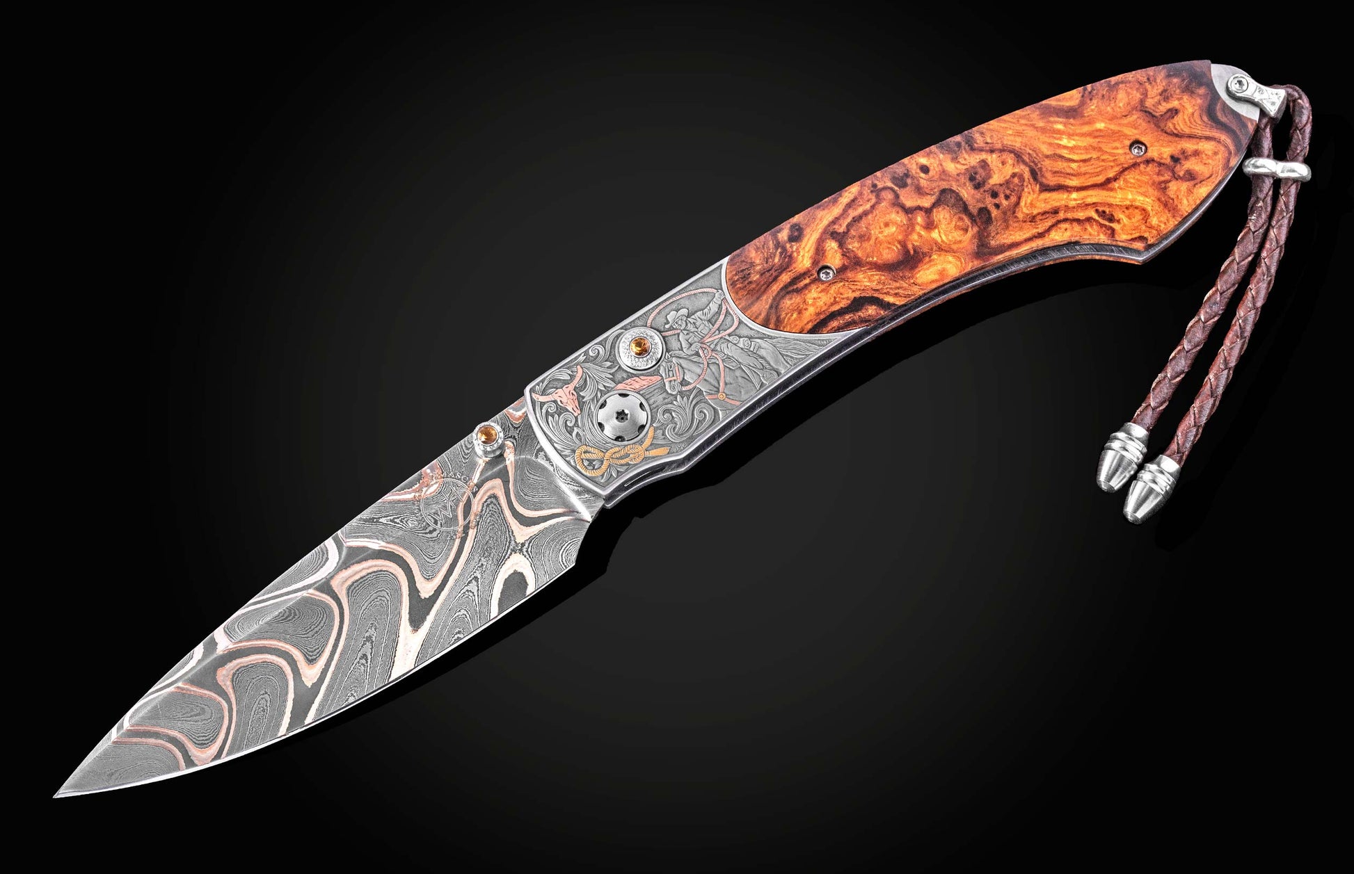 Damascus steel knife with amber wood handle by B12, featuring engraved cowboy motifs and braided leather lanyard, side view on black background