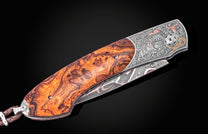 Luxury folding knife with amber burl wood handle and engraved silver bolster featuring cowboy and vaquero artwork, partially open side view