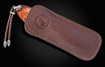 Luxury wooden-handled knife with rich brown leather sheath by B12, featuring embossed logo and braided cord accent, side view.