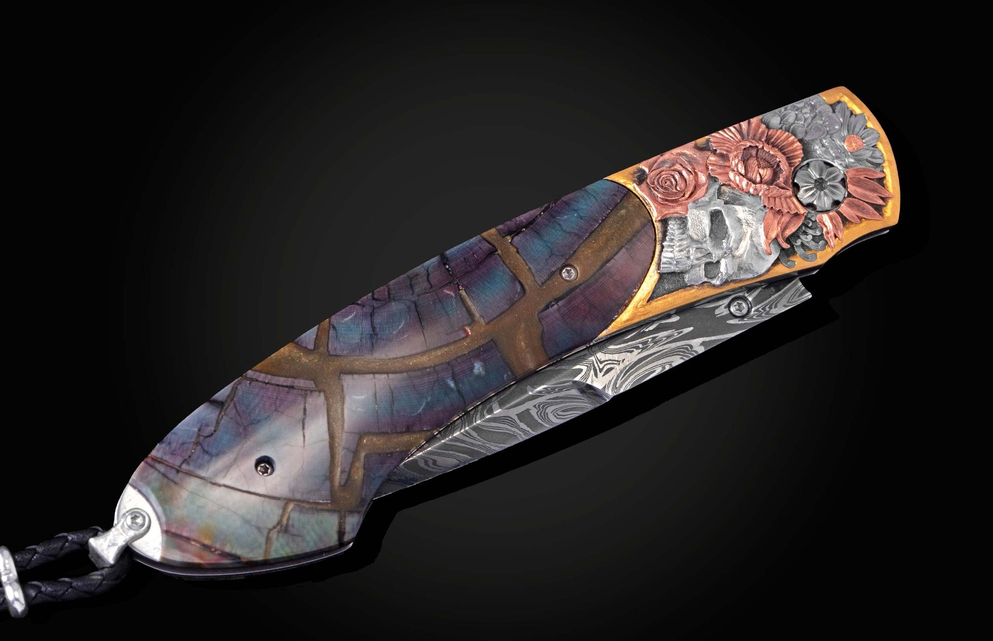 Knife with a mosaic-patterned handle, intricate silver skull and copper floral carvings, a wavy Damascus steel blade, and a black braided leather lanyard.