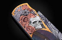 Ornate knife with a handle engraved with a silver skull, copper flowers, gold border, and dark iridescent inlay, featuring a damascus steel blade.