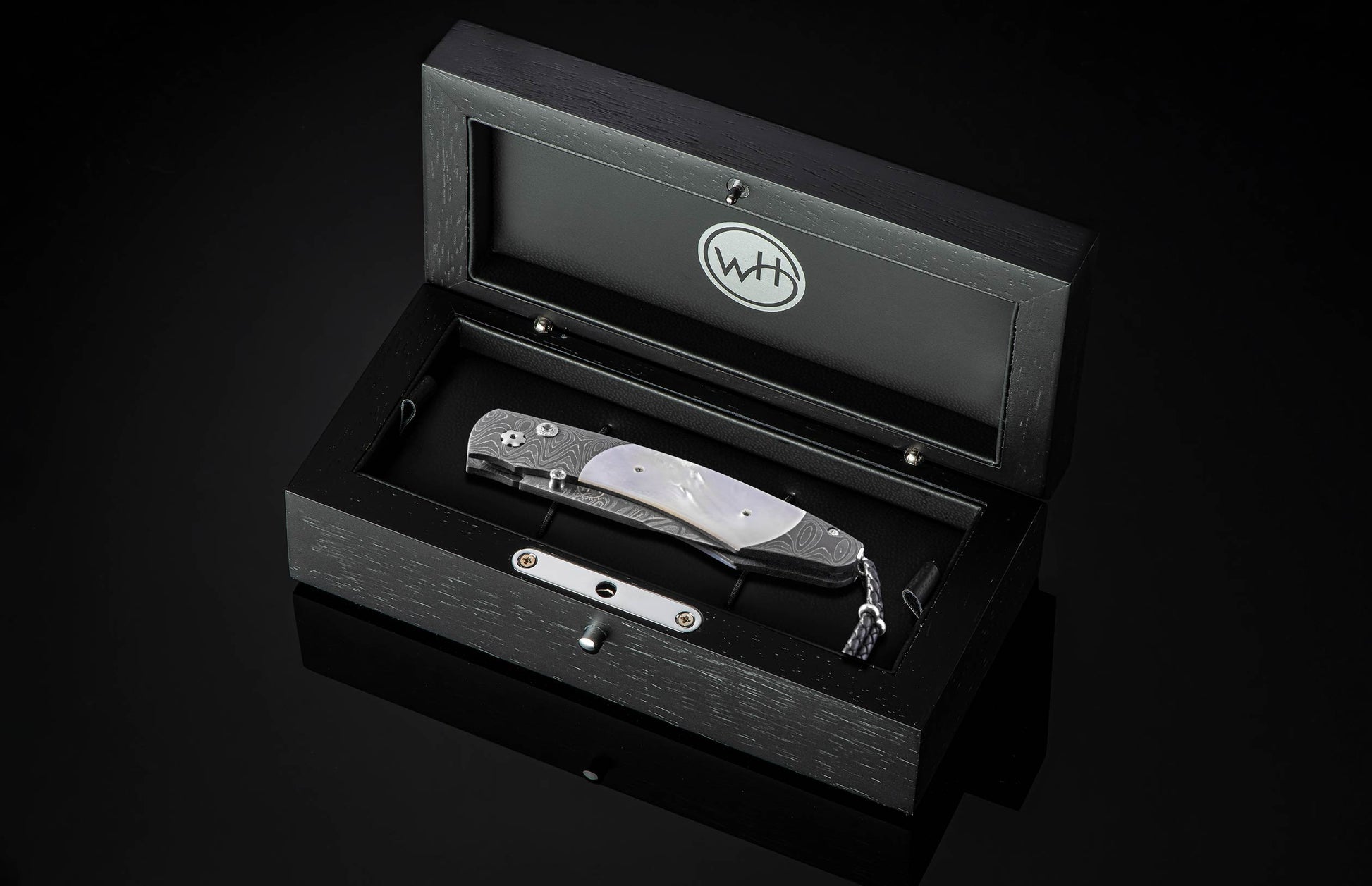 Gilded Ghost folding knife with damascus steel handle and mother-of-pearl inlay by B12, displayed in black wooden presentation box with silver hardware, top-down view