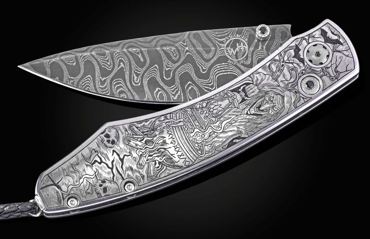 Damascus steel folding knife by B12 with intricate Halloween-themed engraving, silver-toned handle, and black gem accents, displayed open on black background