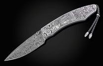 Luxury damascus steel knife with intricate Halloween-themed engravings on silver handle, featuring braided cord and polished hardware, side view on black background