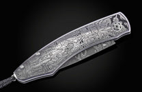 Luxury folding knife with intricate Halloween-themed engraving, featuring zombies and haunted scenes, by B12, silver-toned metal with damascus blade, side view on black background