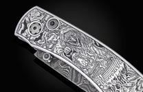 Silver folding knife with intricate Halloween-themed engraving featuring a witch, bats, and occult symbols, side view on black background