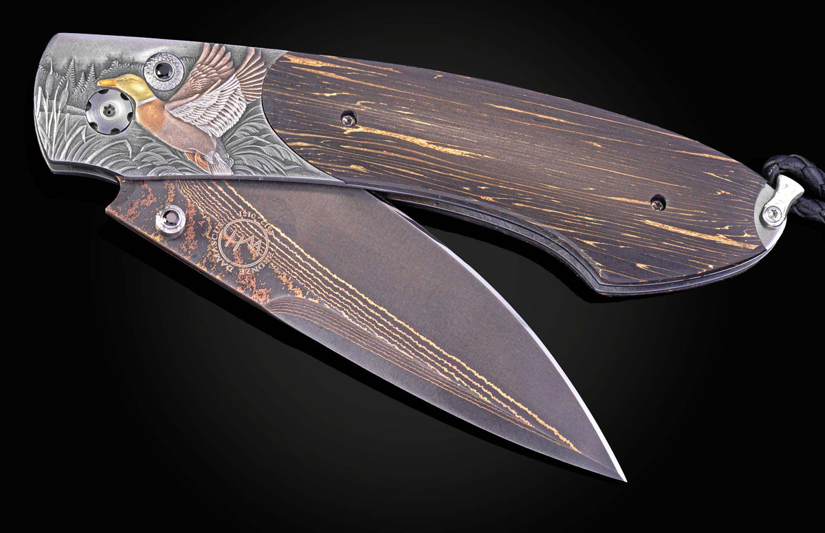 Folding knife with a dark wood handle and an engraved metal bolster featuring a golden-headed mallard duck, dark gems, and a bronze Damascus patterned blade.