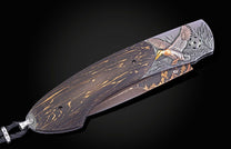 Decorative folding knife with dark wood handle, golden streaks, and a detailed metal engraving of a mallard duck with gold and bronze accents flying over reeds.